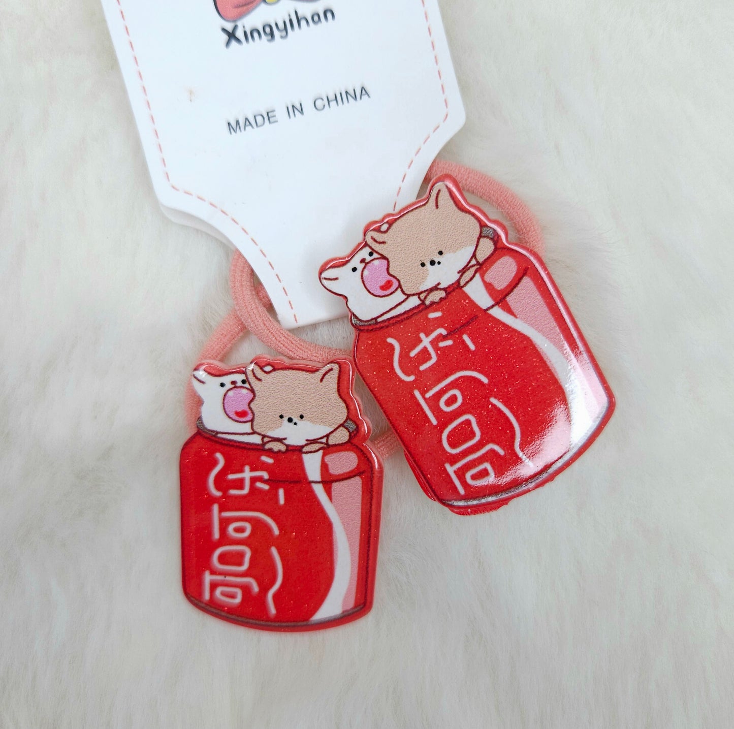 Two red cat-shaped hair ties with cartoon cats on a beige background, featuring a 'Made in China' label.