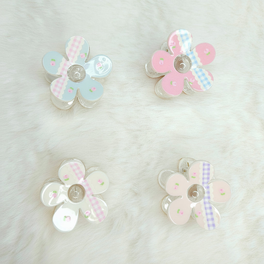 Four pastel-colored flower-shaped kawaii hair claws displayed on soft background.