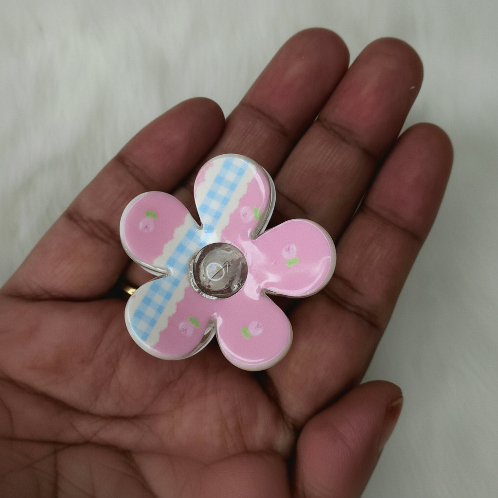 Close-up of glossy white flower hair claw decorated with pink gingham stripe and rose motifs for reference.