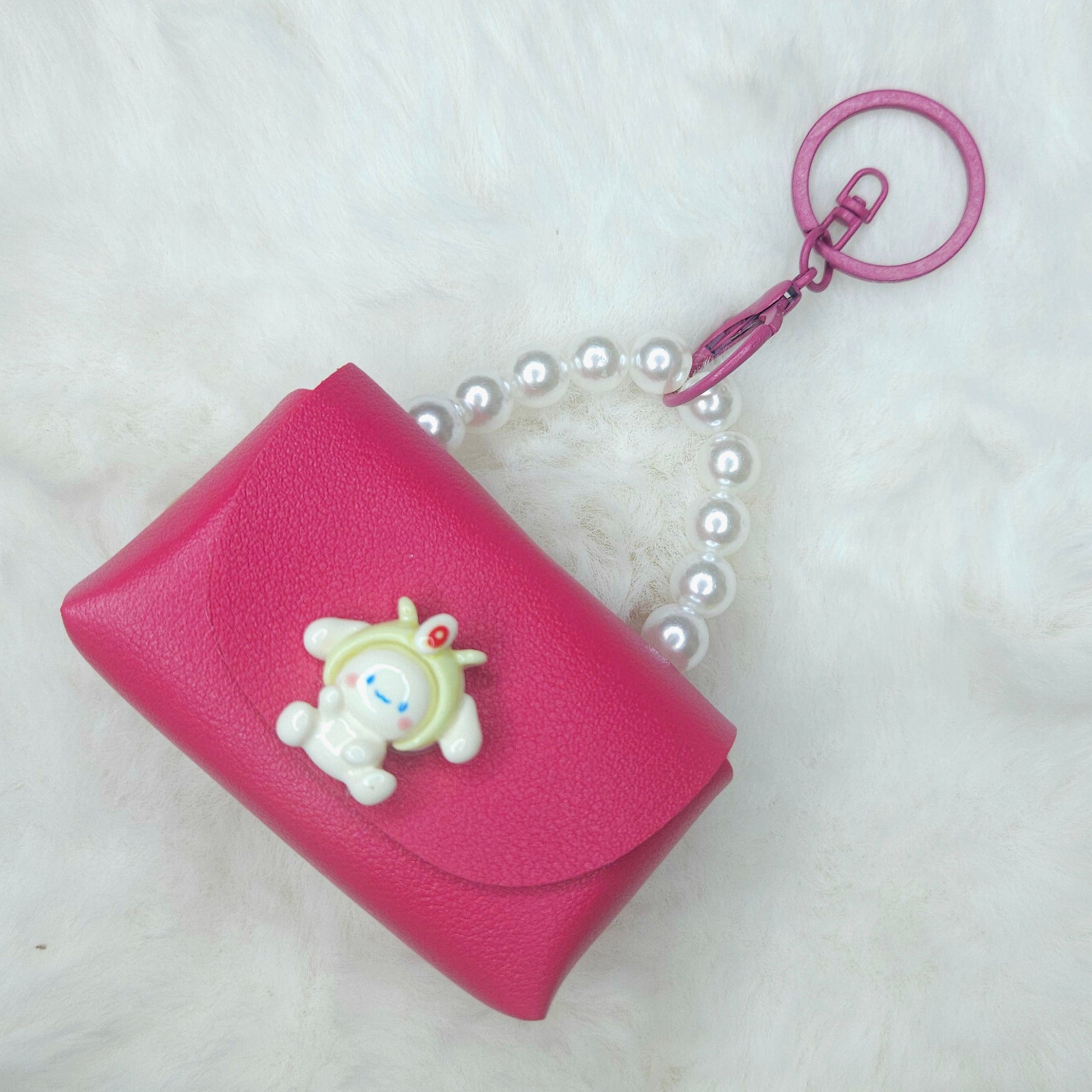 Pink wallet with a cartoon character charm and pearl necklace on a white background