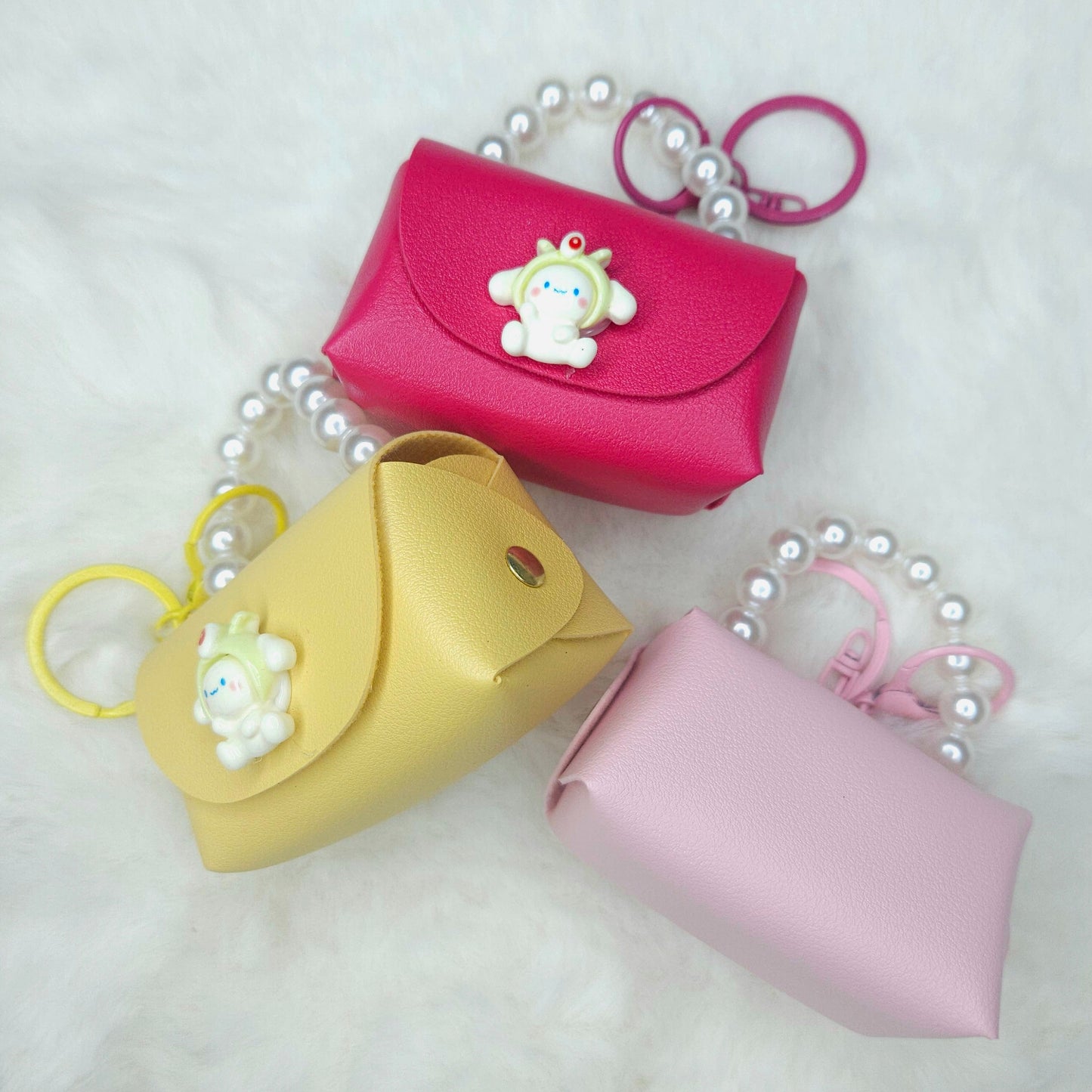 Three small pouches in pink, yellow, and pink with a keychain on a white background