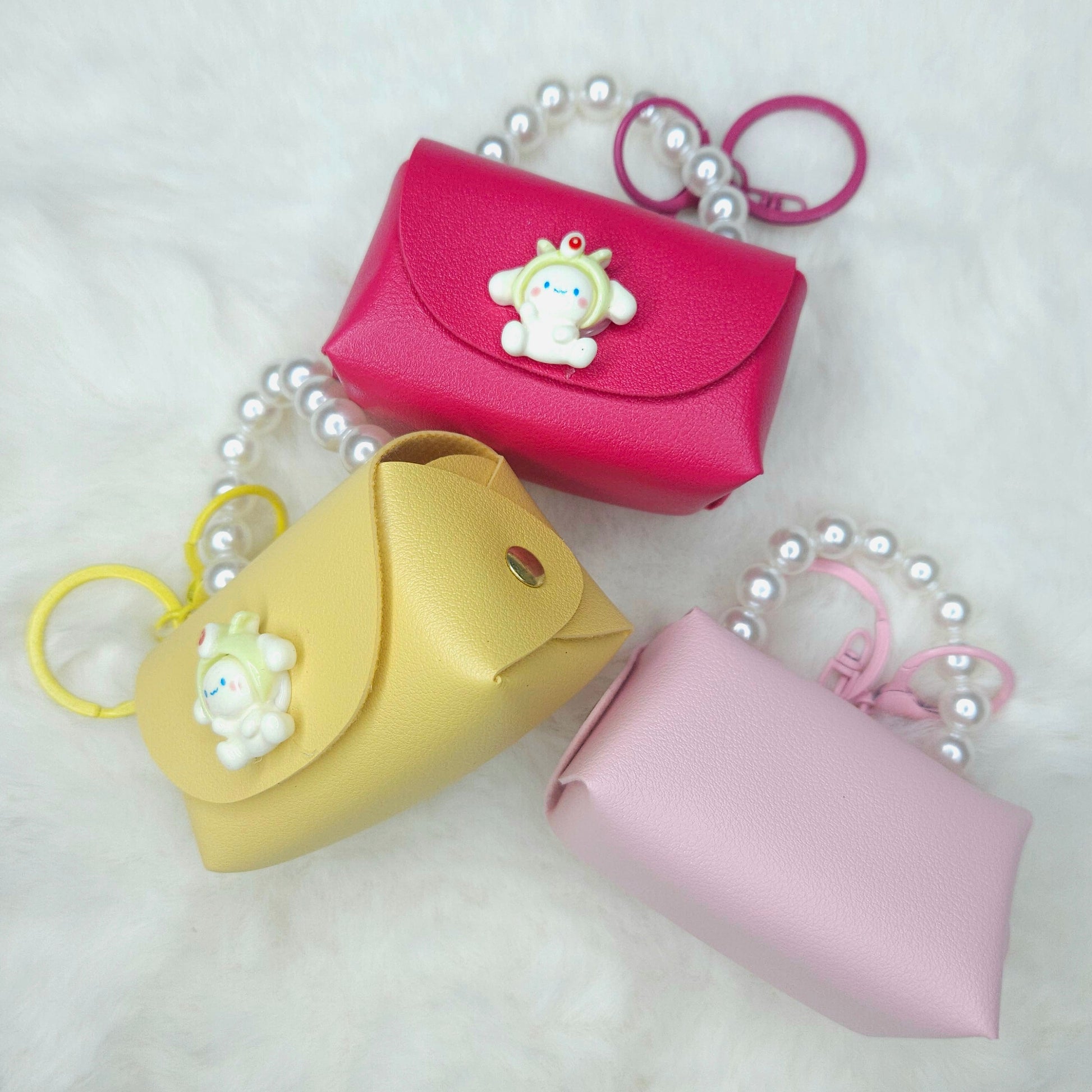 Three small pouches in pink, yellow, and pink with a keychain on a white background