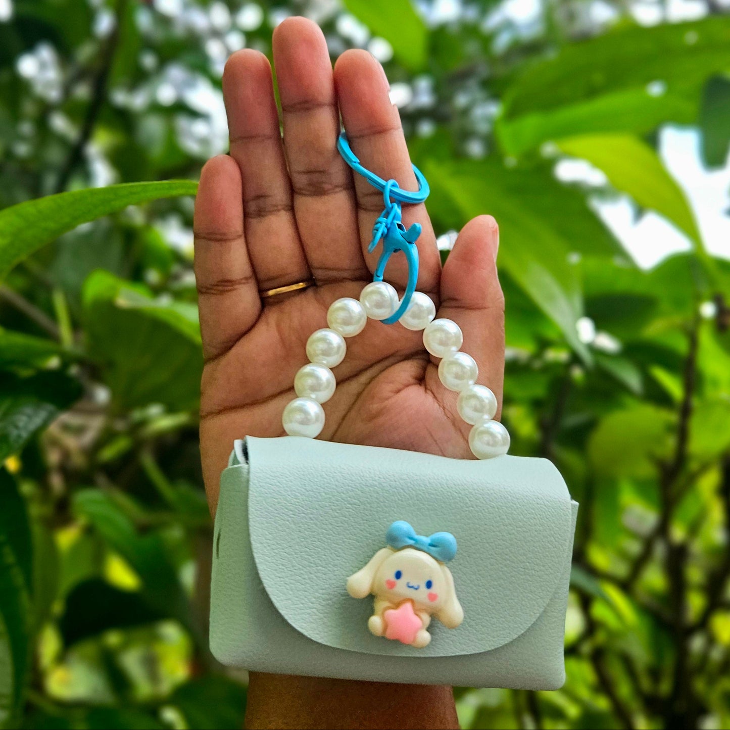 Light blue pouch with a cartoon character held by a hand against a green leafy background