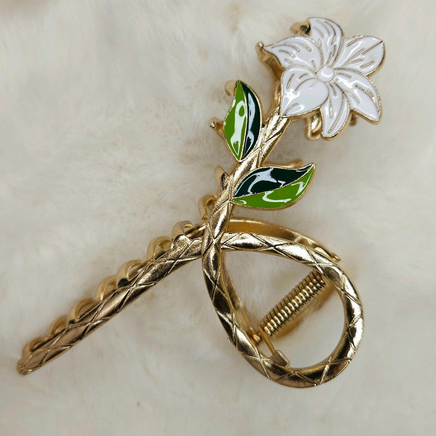 Gold metal hair claw with a white flower and green leaves on a beige background