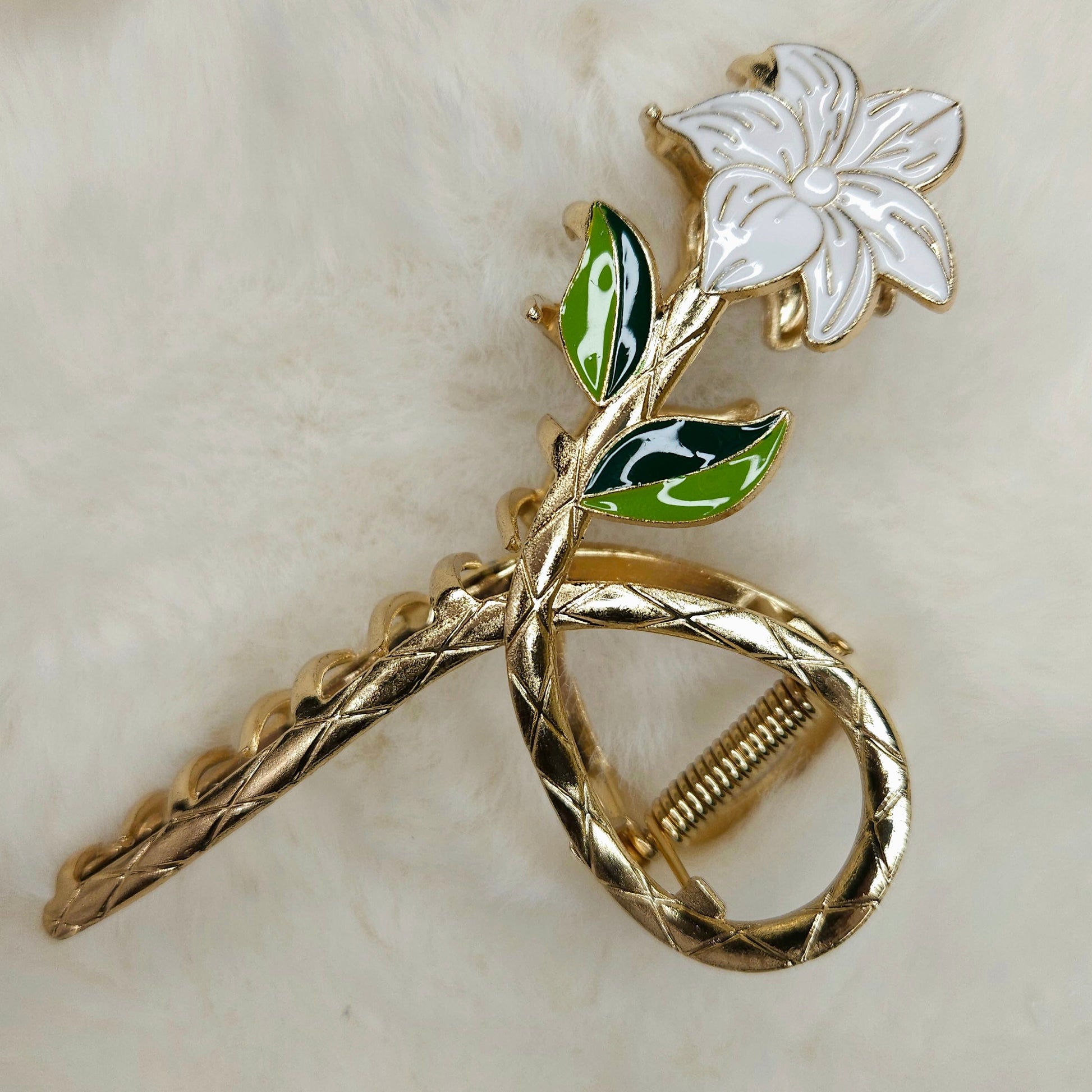 Gold metal hair claw with a white flower and green leaves on a beige background