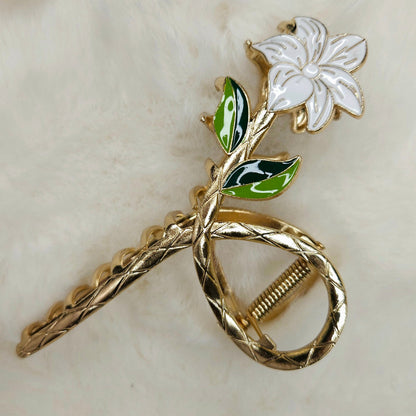 Gold metal hair claw with a white flower and green leaves on a beige background