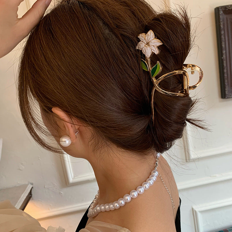 Woman with elegant hair bun adorned with a decorative hair clip, wearing a pearl necklace.