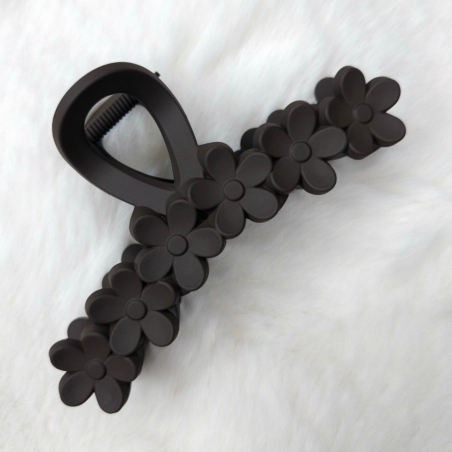 Black flower-detailed hair claw clip on a white fabric background