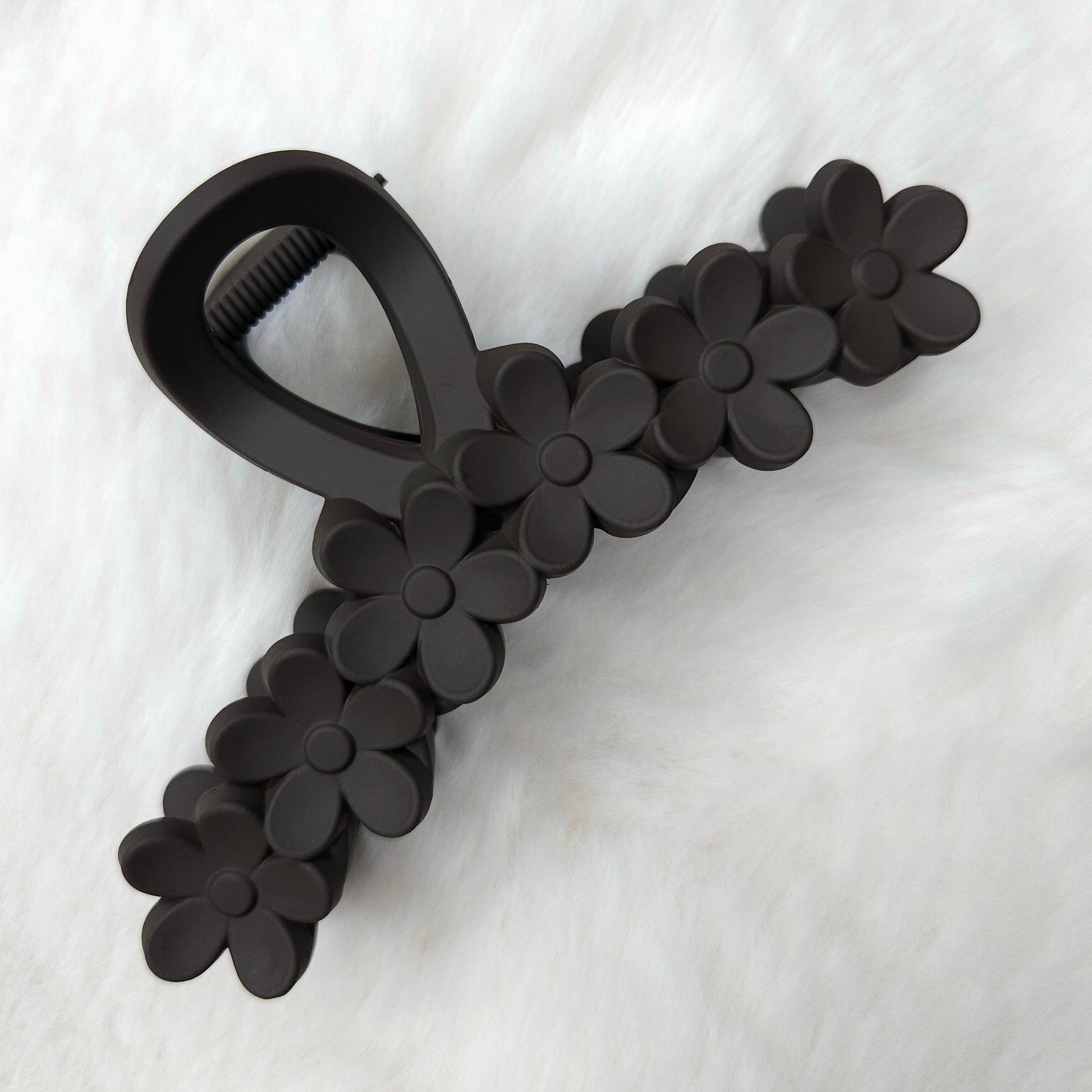 Black flower-detailed hair claw clip on a white fabric background