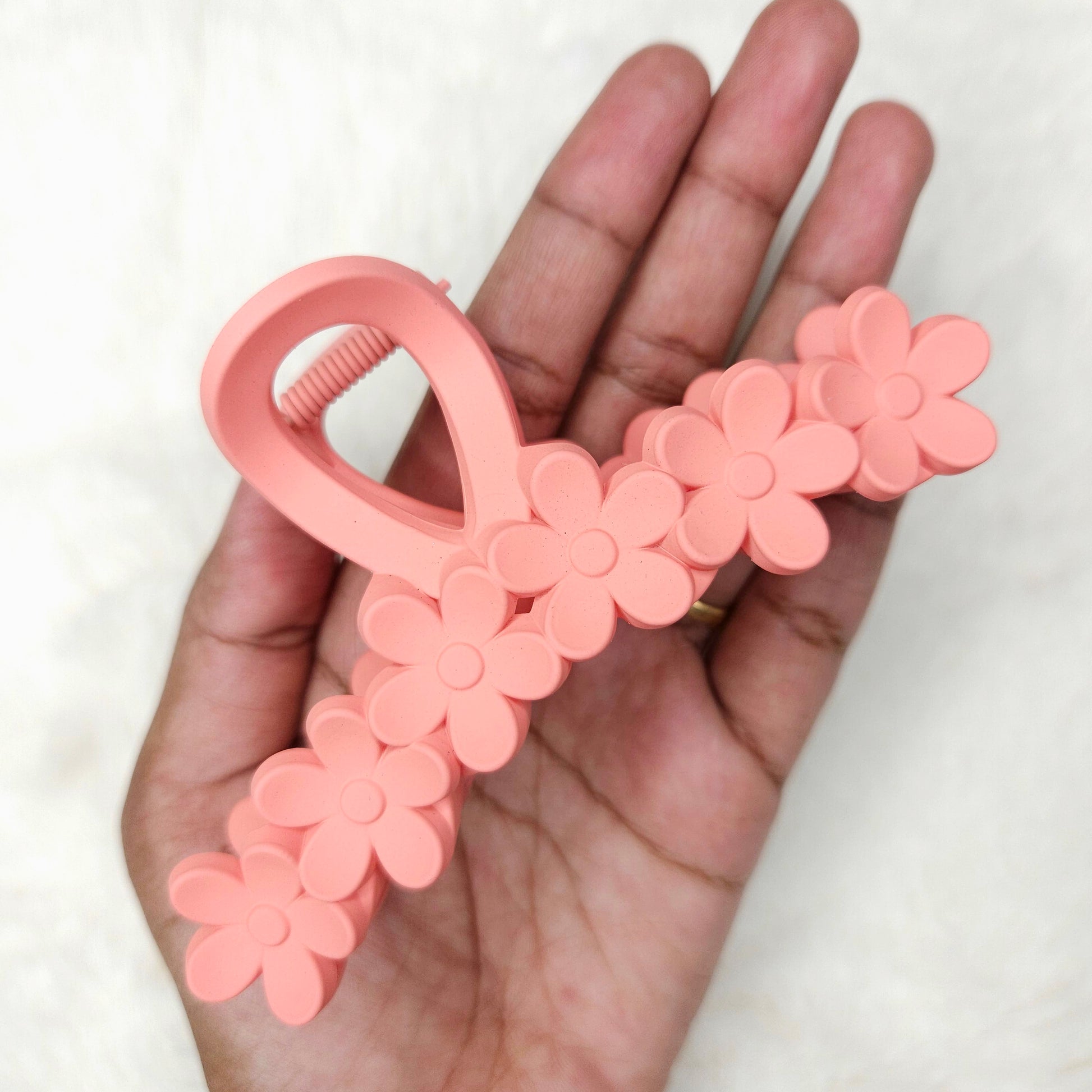 Pink floral hair clip held in a hand against a white background