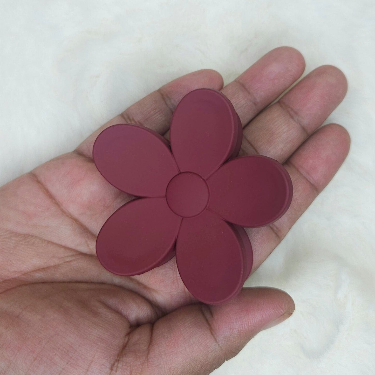 Hand holding a maroon flower-shaped hair claw against a white background