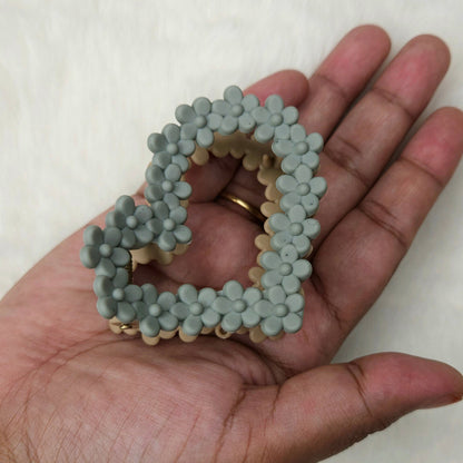 Hand holding two gray beaded floral hair claw against a white background
