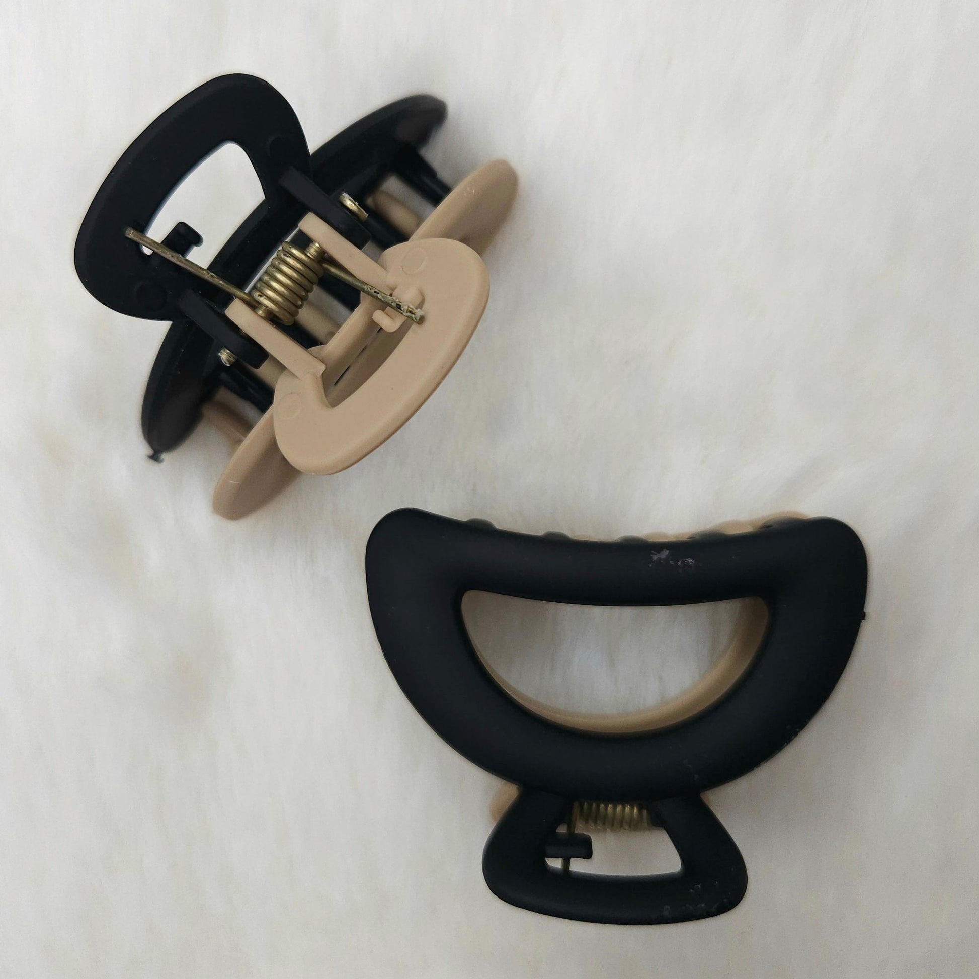 Two hair clips, one black and one beige, on a white background