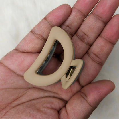Beige hair claw clip in a hand against a white background