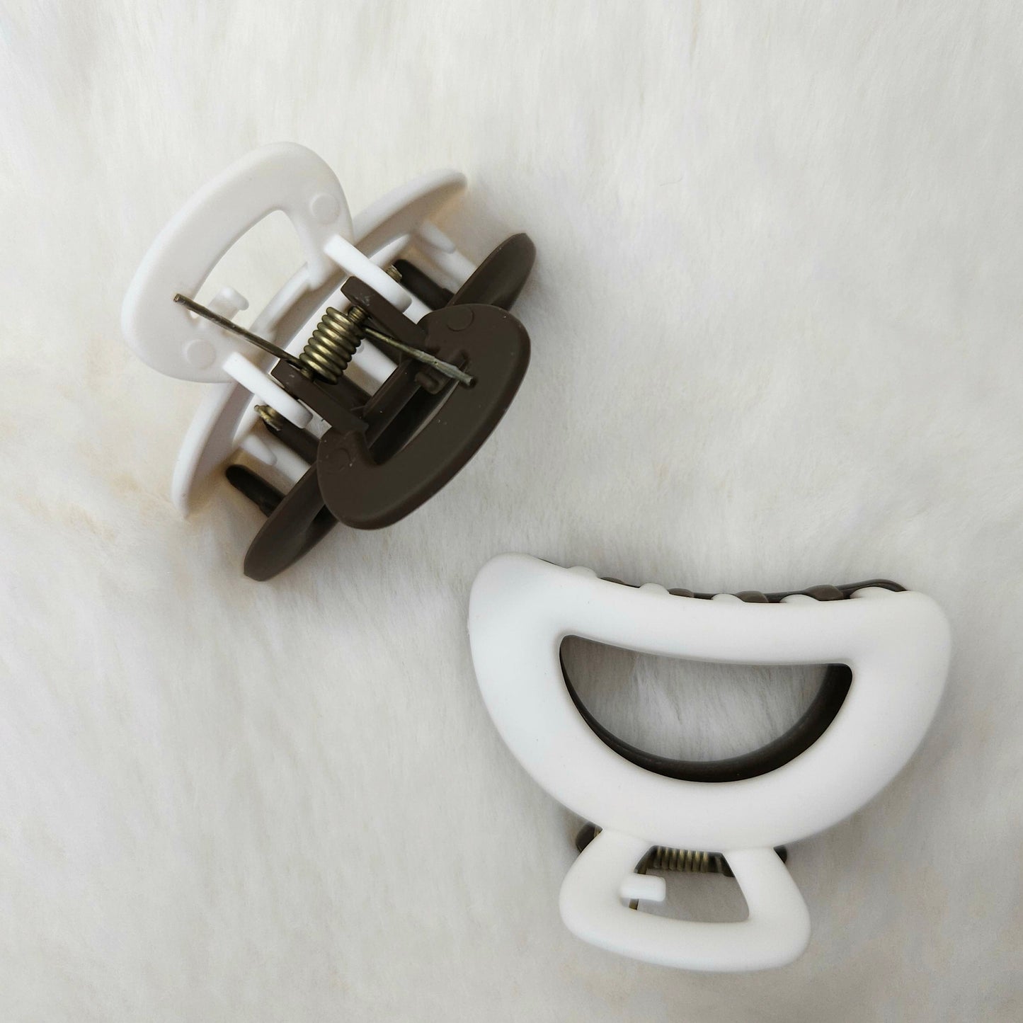 Two hair clips, one white and one black, on a white fur surface.