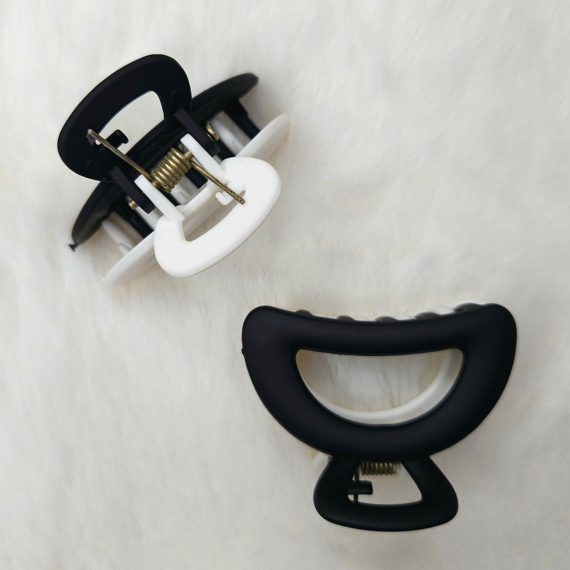 Two hair clips, one black and one white, on a textured white background