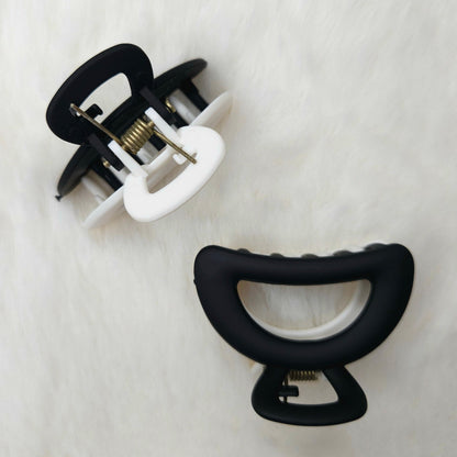 Two hair clips, one black and one white, on a textured white background