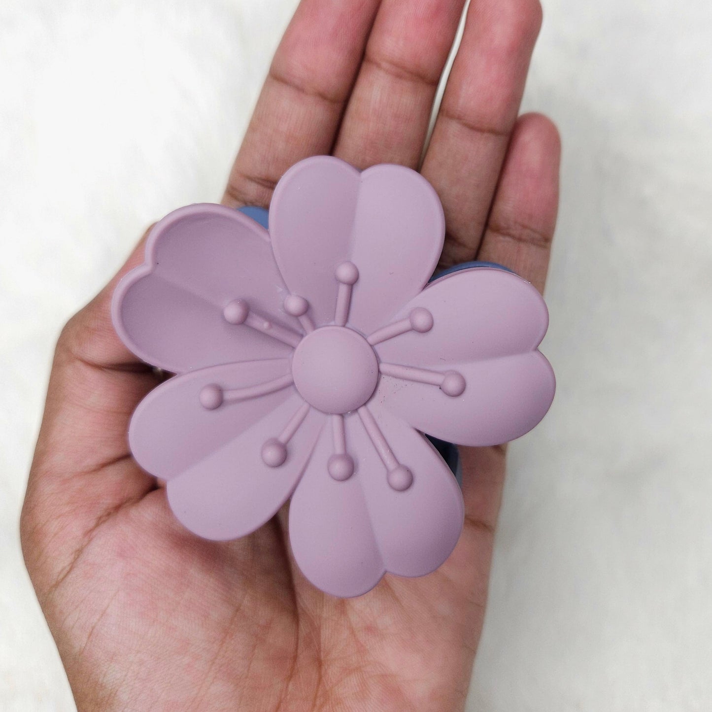 Hand holding a purple flower-shaped hair claw clip against a white background
