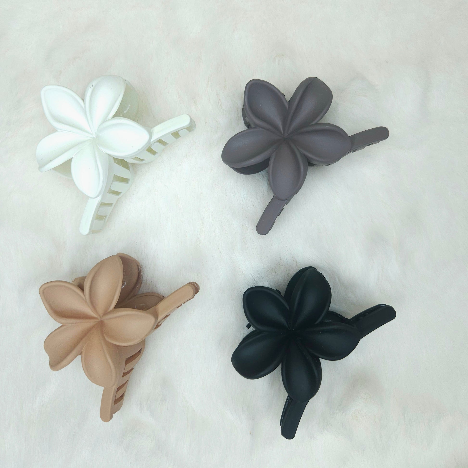 Four floral-shaped hair clips in white, gray, beige, and black on a light background.