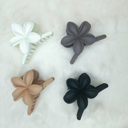 Four floral-shaped hair clips in white, gray, beige, and black on a light background.