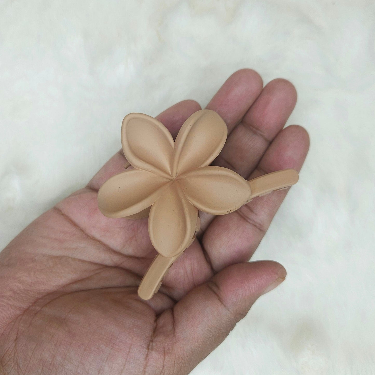 Hand holding a beige flower-shaped hair claw against a white background