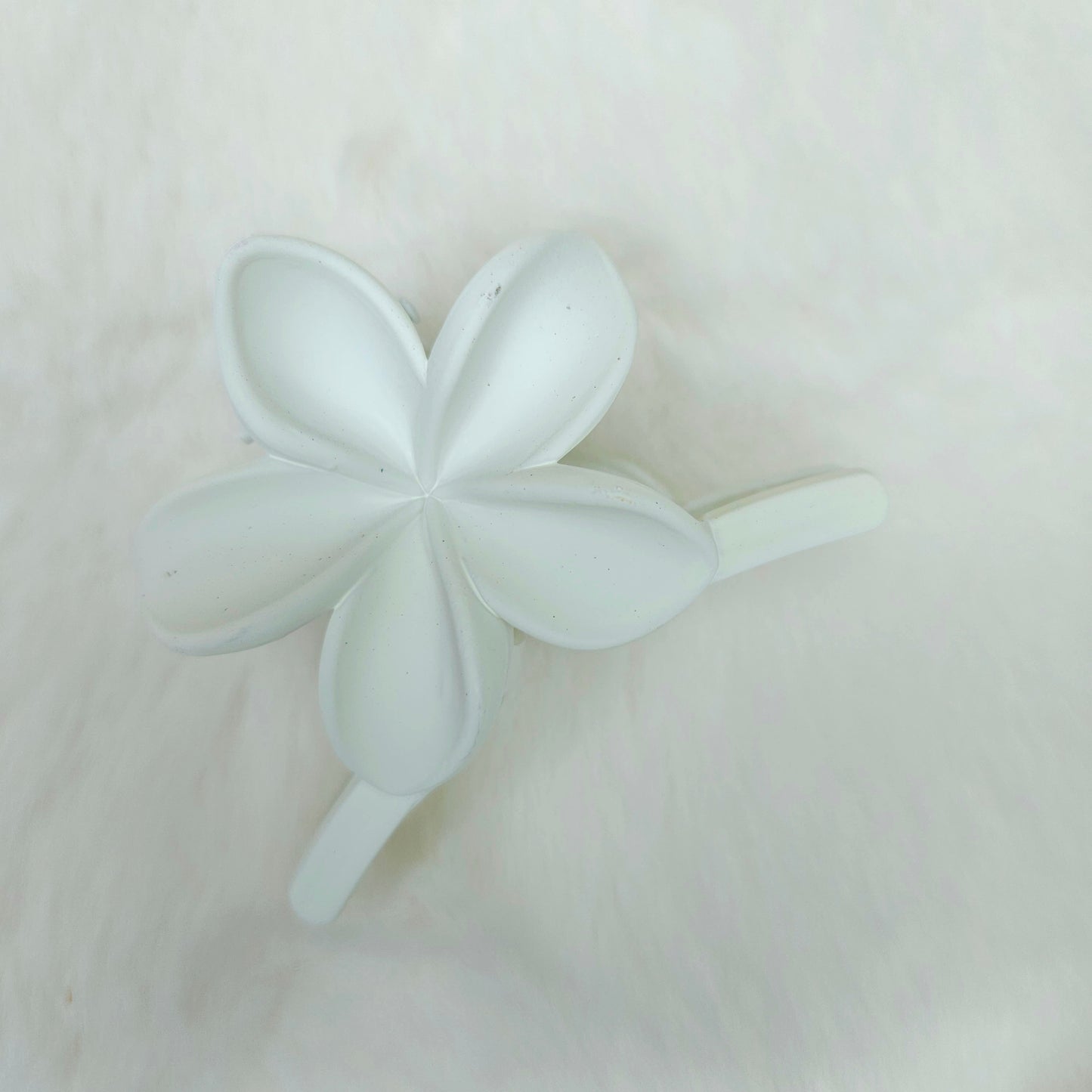 White flower-shaped hair claw on a light pink background