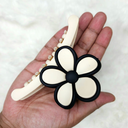 Hand holding a hair clip with a black and white flower design on a white background