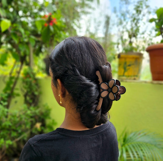 Person with a styled hair bun wearing a floral hair clip, standing outdoors with greenery in the background.
