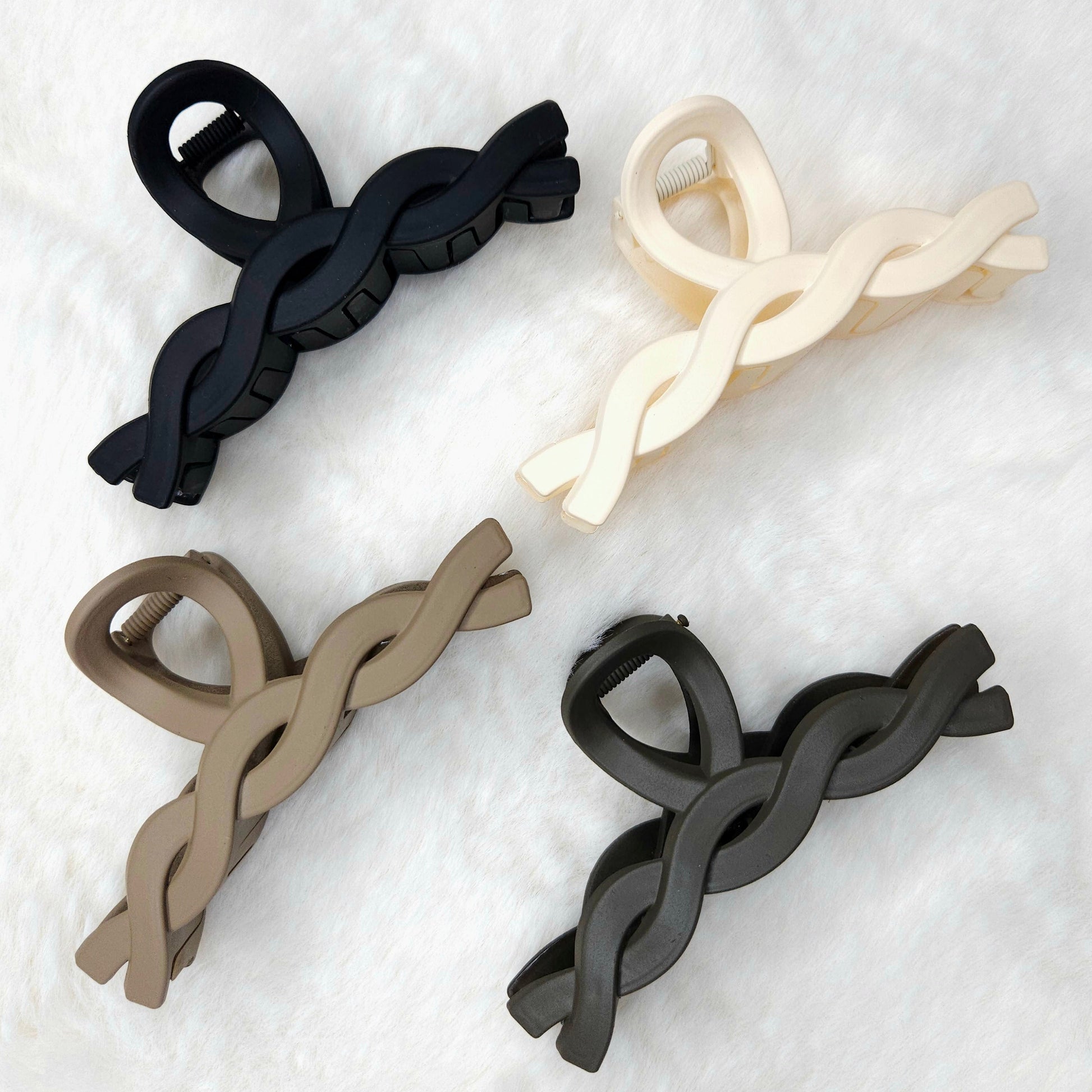 Four hair clips in black, beige, and white on a textured white background