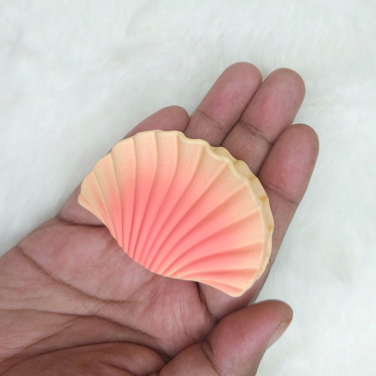 Hand holding a pink shell-shaped hair claw against a white background
