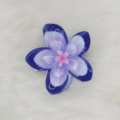 A blue and white translucent plastic flower-shaped hair clip with a light blue center, seen from above, with the clip mechanism slightly visible underneath.