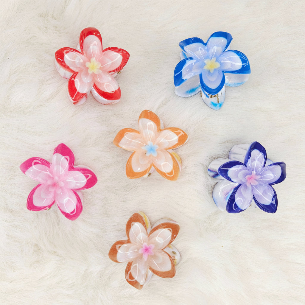 Six colorful translucent plastic flower-shaped hair clips are arranged on a white fluffy surface. From left to right, top row: red and white, blue and white. Middle row: pink and white, orange and white, purple and white. Bottom row: brown and white.
