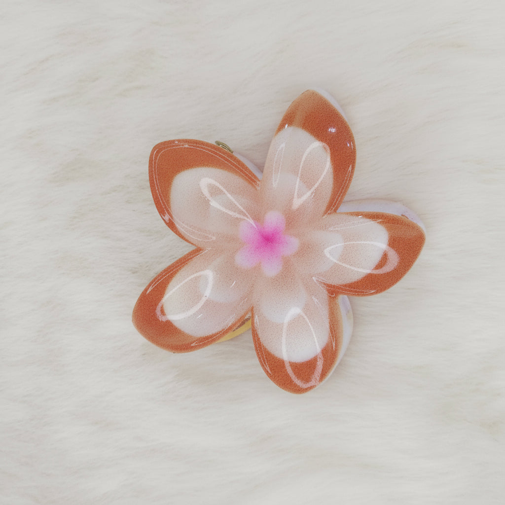 An orange and white translucent plastic flower-shaped hair clip with a light blue center, seen from above.