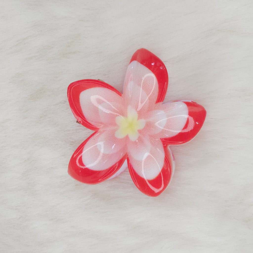 An orange and white translucent plastic flower-shaped hair clip with a light blue center, seen from above.