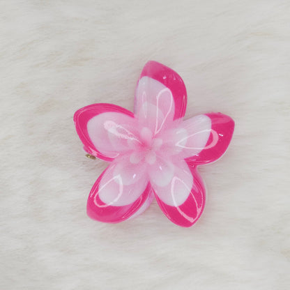 A pink and white translucent plastic flower-shaped hair clip with a light pink center, seen from above.