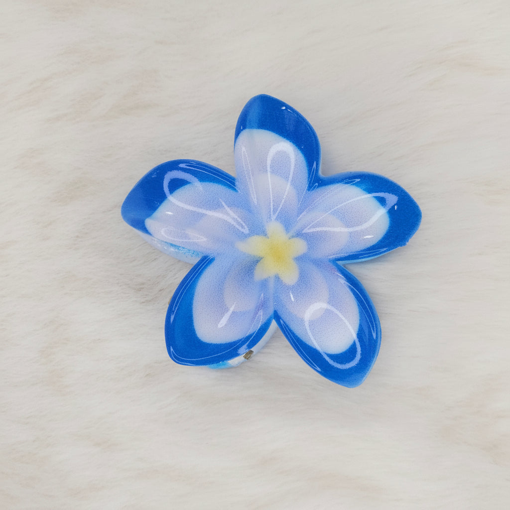 A sky-blue and white translucent plastic flower-shaped hair clip with a light blue center, seen from above, with the clip mechanism slightly visible underneath.