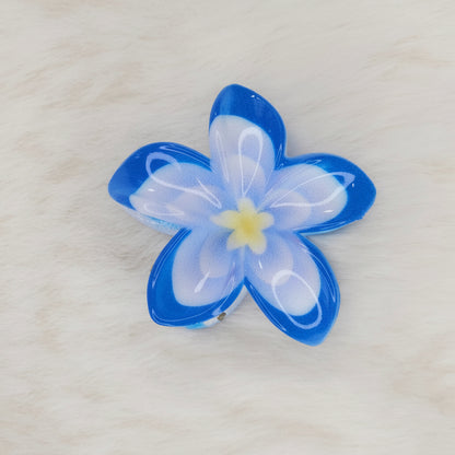 A sky-blue and white translucent plastic flower-shaped hair clip with a light blue center, seen from above, with the clip mechanism slightly visible underneath.