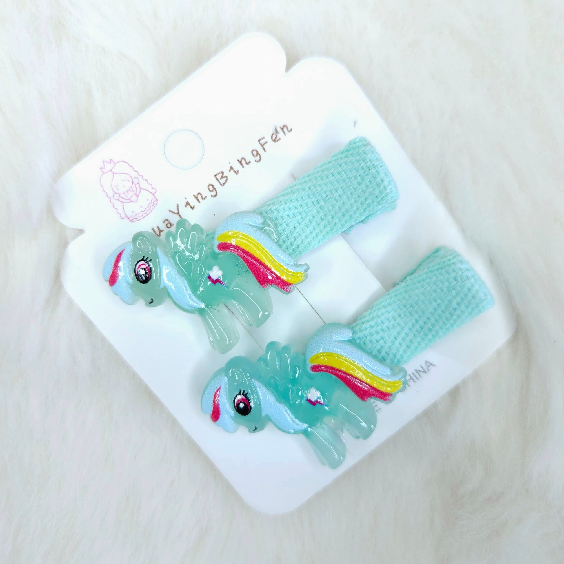 Pair of green animal-themed hair ties in a white packaging on a light background