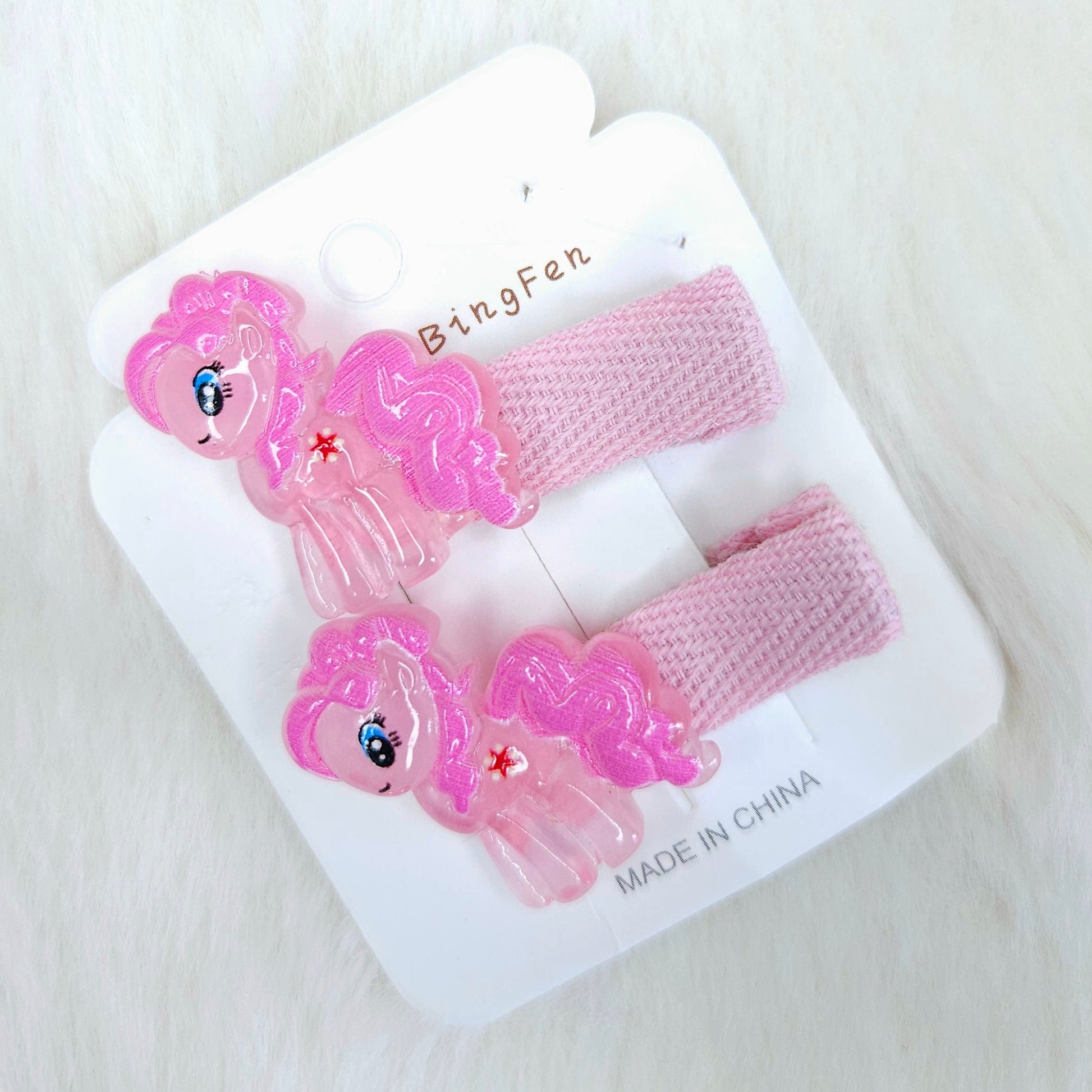 Set of pink hair clips with cartoon character design on a white card, placed on a white surface.
