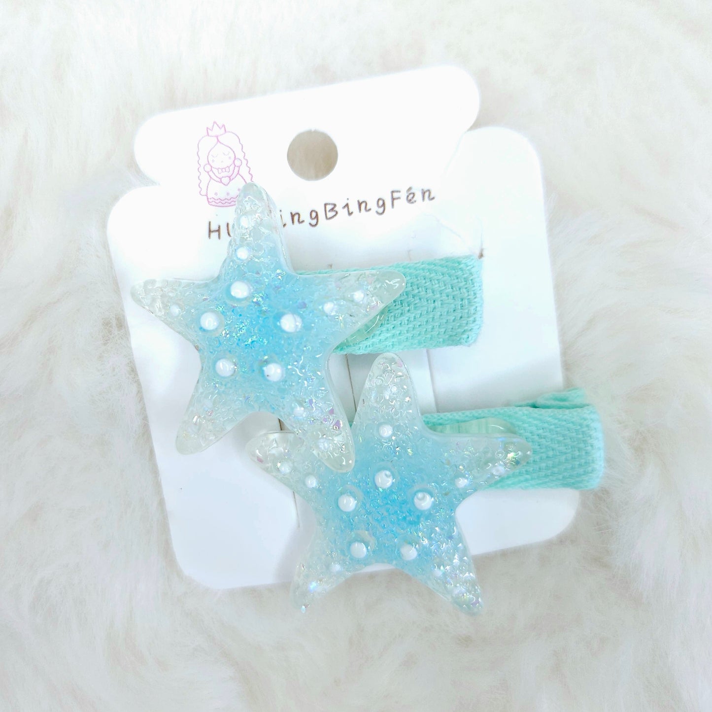 Pair of blue star-shaped hair clips on a white card with 'Hi Bingfen' branding, on a white fluffy background.