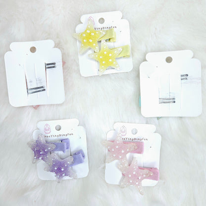 Set of star-shaped hair clips on white cards with visible brand name on a light background