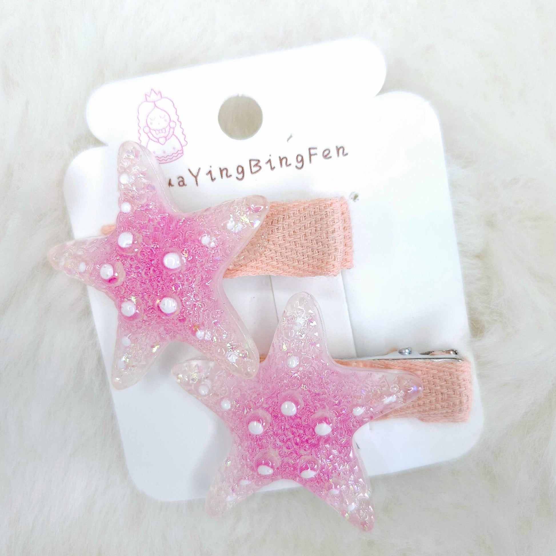 Pink star-shaped hair clips on a white card with 'YingBingFen' branding, placed on a white fluffy surface.