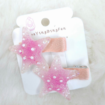 Pink star-shaped hair clips on a white card with 'YingBingFen' branding, placed on a white fluffy surface.