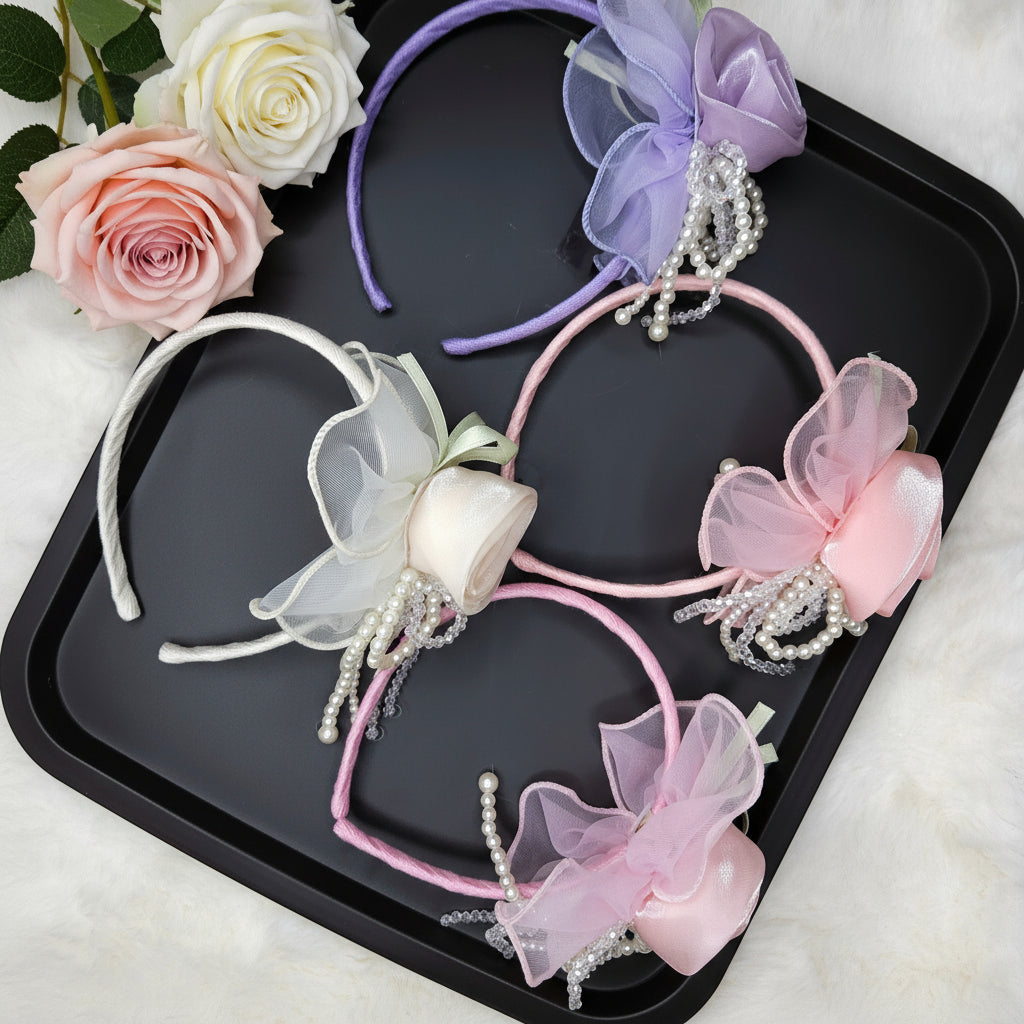 Four decorative headbands with flowers and pearls on a black tray, surrounded by roses.
