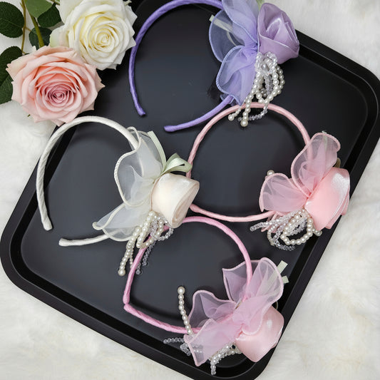Four decorative headbands with flowers and pearls on a black tray, surrounded by roses.