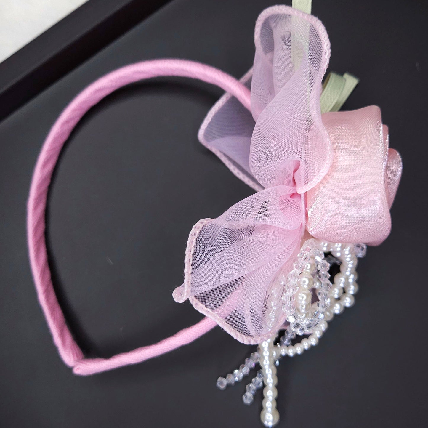 Pink headband with bow and beads on a black surface