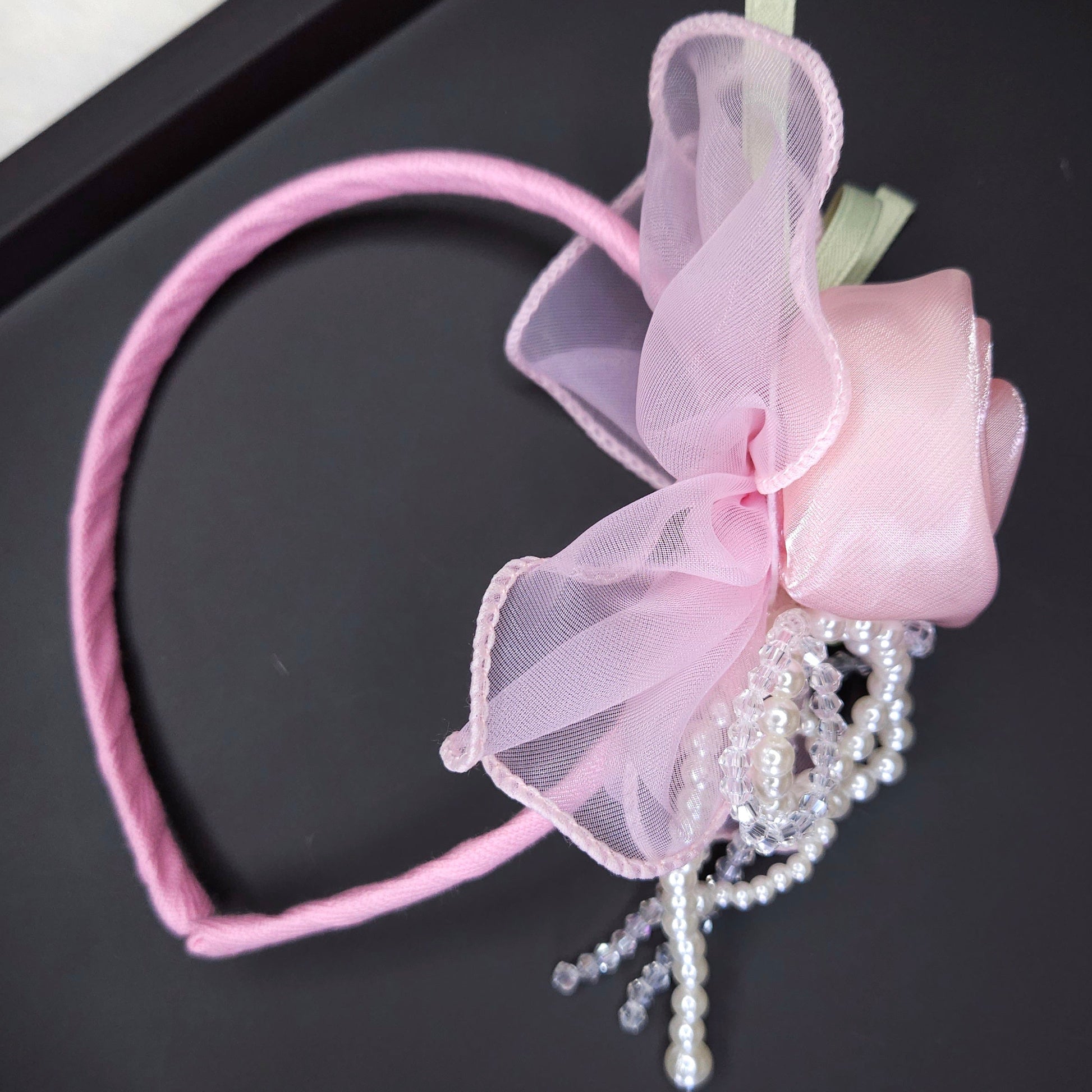 Pink headband with bow and beads on a black surface