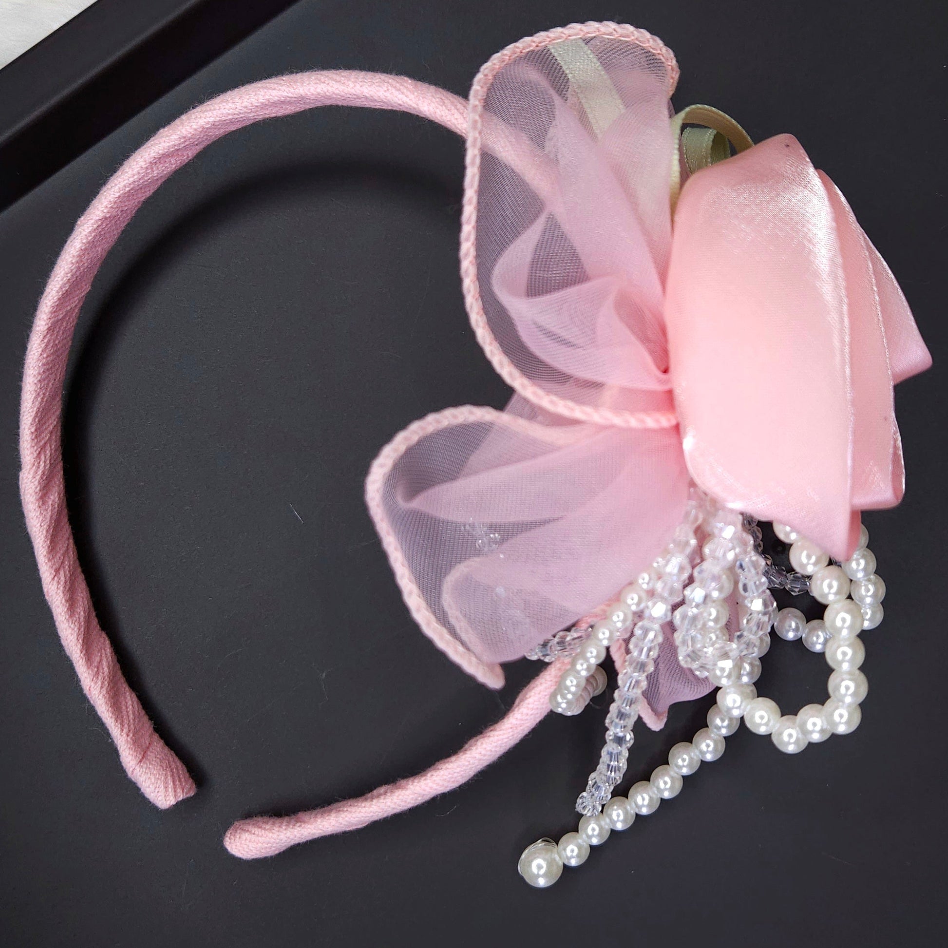 Pink headband with a bow and pearl decorations on a black surface