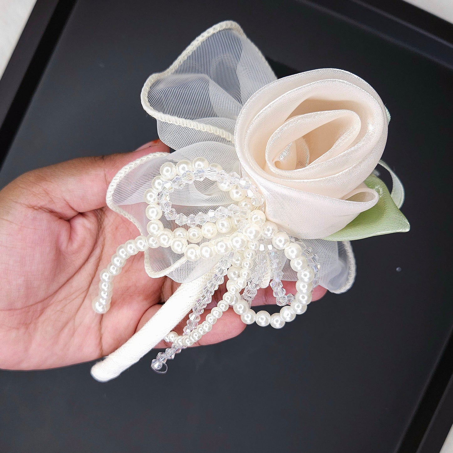 Hand holding a decorative flower headband with pearls on a black tray