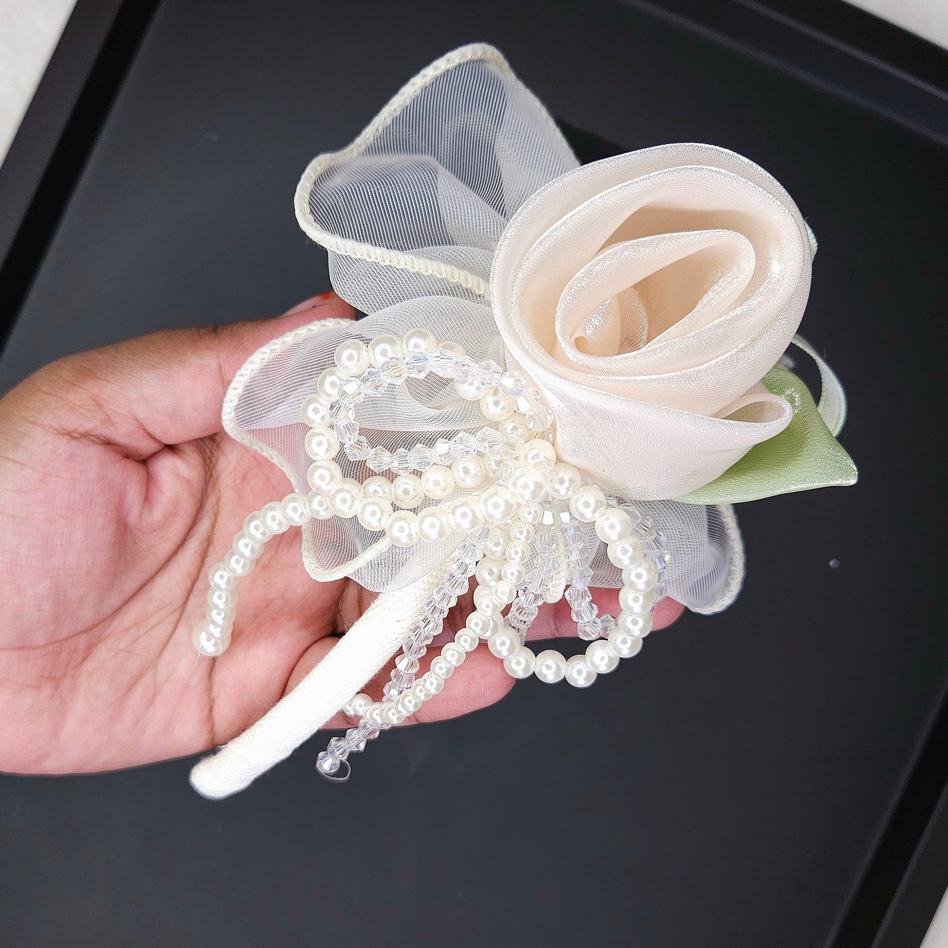 Hand holding a decorative flower headband with pearls on a black tray